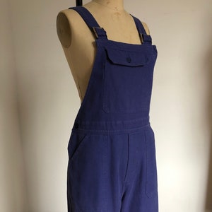 K&ouml;nnte beinhalten: Eine blaue Denim-Latzhose mit einer Brusttasche und zwei Seitentaschen.