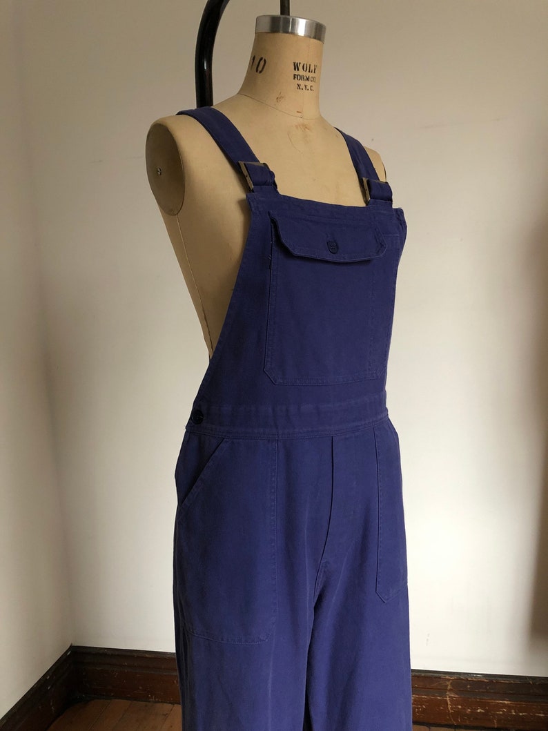 K&ouml;nnte beinhalten: Eine blaue Denim-Latzhose mit einer Brusttasche und zwei Seitentaschen.
