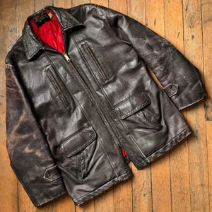 May include: A brown leather jacket with a zip fastening and multiple pockets. The jacket has a red lining and a worn appearance.