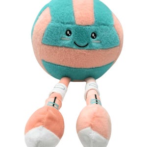 May include: A plush toy volleyball with a smiling face, teal and peach stripes, and attached legs. The legs are peach with white tips and teal accents. The toy is designed to resemble a friendly character.