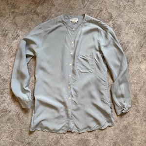 May include: A light blue long-sleeve button-down shirt with a mandarin collar, a single chest pocket, and a curved hem. The shirt features a front button placket with light-colored buttons and an Ann Taylor brand label at the inner neckline.