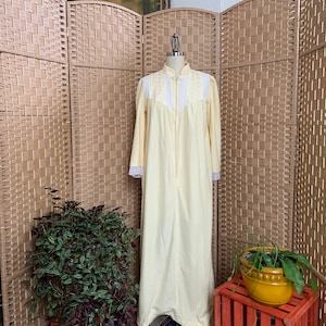 May include: A pale yellow nightgown with white lace trim and a zipper closure. The nightgown is on a mannequin in front of a wicker screen.