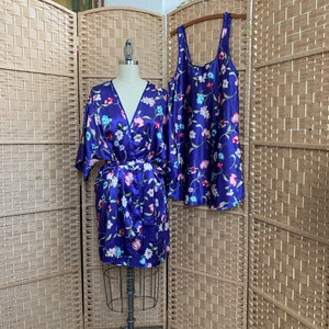 May include: A purple satin robe and matching slip with a floral print. The robe has long sleeves and a tie belt. The slip has thin straps.