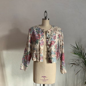 May include: A white floral patterned cropped jacket with a button closure. The jacket has a pink, blue, and green floral pattern.
