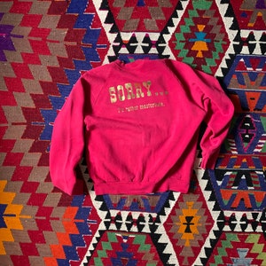 May include: A bright pink sweatshirt with the word "SORRY" in gold lettering across the chest. Below the word "SORRY" is the phrase "I'd rather masturbate." The sweatshirt is made of a soft material.