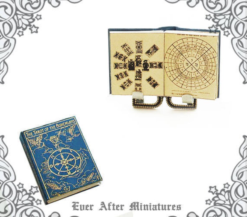 May include: A miniature book titled "The Tarot of the Bohemians" with a blue cover and gold accents. The book is open to reveal a detailed illustration of a tarot card. The book is sitting on a white surface.
