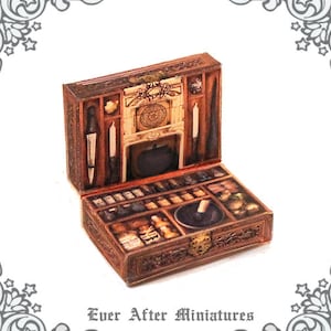 May include: A miniature wooden box with a hinged lid, open to reveal a detailed interior with compartments and a small fireplace. The box is decorated with a brown and gold paint scheme and features a variety of miniature items, including bottles, jars, and a mortar and pestle.