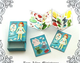 May include: A vintage Suzy Doll Book with a blue cover and a doll with red hair and a blue dress. The book is open to show the different outfits the doll can wear. The book is in a blue box with the words "Suzy Doll Book" on the front.