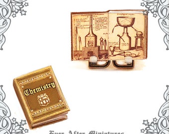 May include: Two miniature books, one titled "Chemistry" in gold lettering on a gold background, and the other with an illustration of a chemistry experiment in brown and white. The books are on a white background.