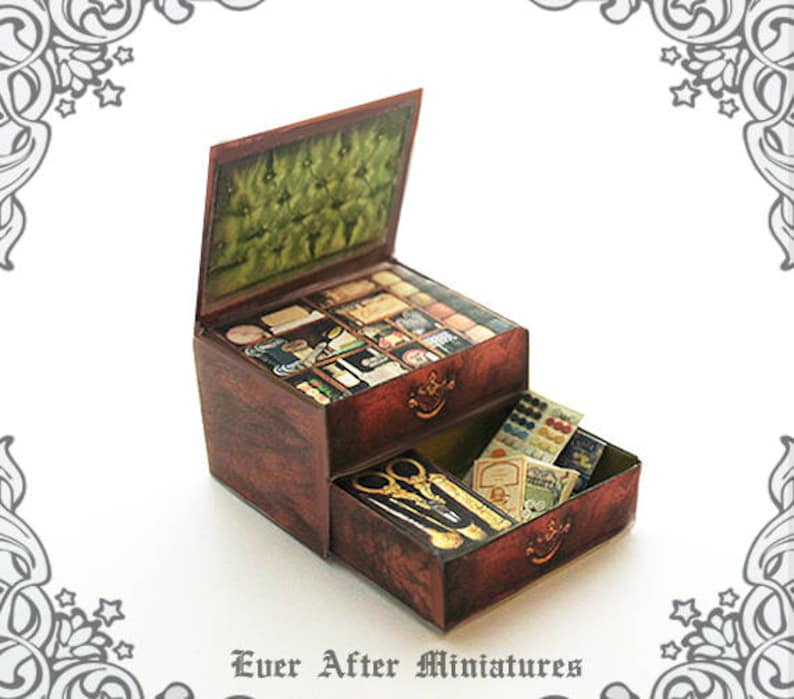 Puede incluir: Una caja de madera de dos niveles con una tapa con bisagras, llena de art&iacute;culos en miniatura. La caja est&aacute; decorada con un patr&oacute;n floral y tiene una manija de lat&oacute;n. El nivel superior est&aacute; lleno de art&iacute;culos de costura en miniatura, mientras que el nivel inferior est&aacute; lleno de botones y cuentas en miniatura. La caja est&aacute; etiquetada como "Ever After Miniatures".
