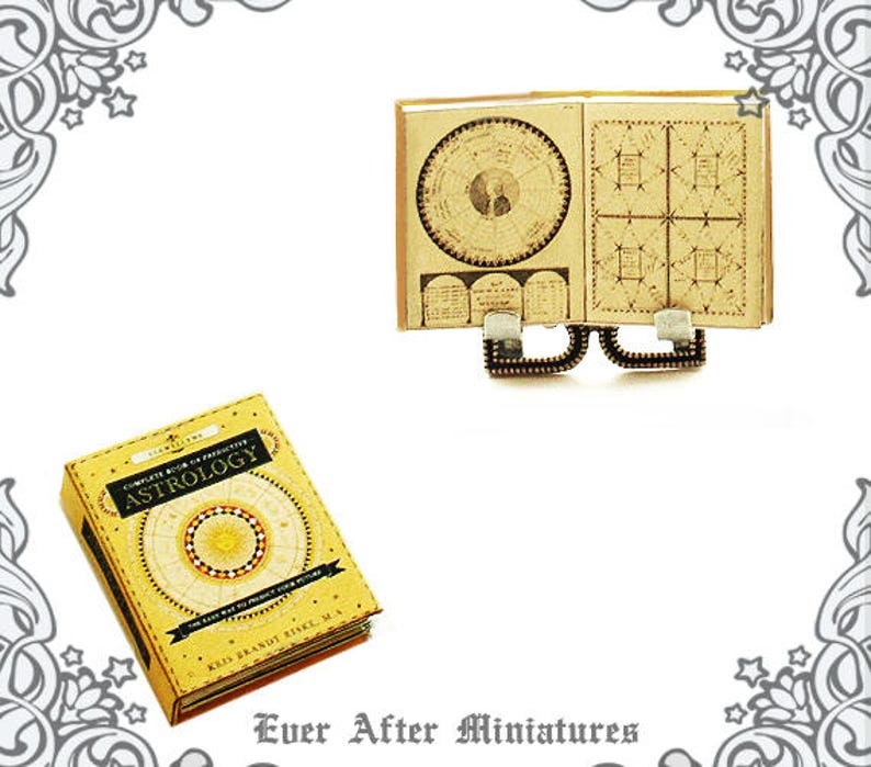 May include: A miniature book titled "Complete Book of Predictive Astrology" with a yellow cover and gold accents. The book is open to a page with a circular chart and a grid pattern. The book is on a miniature stand with a gold finish.