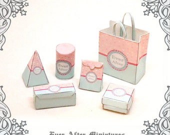 Könnte beinhalten: Ein Set aus Miniatur-Papierbastelboxen und -taschen in einem hellblauen und rosafarbenen Farbschema. Die Boxen und Taschen tragen den Text "Ever After" in einem dekorativen Kreis. Die Boxen haben verschiedene Formen, darunter eine Pyramide, ein Zylinder und eine rechteckige Box. Die Taschen sind eine Einkaufstasche und eine kleine Tasche im Briefumschlag-Stil.