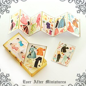 May include: A set of miniature paper dolls with various outfits and accessories. The dolls are in a vintage style and come in a small box with a gold trim. The box has the text "Ever After Miniatures" printed on the bottom.