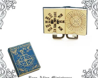 May include: A miniature book titled "The Tarot of the Bohemians" with a blue cover and gold lettering. The book is open to a page with a circular design and is displayed on a miniature book stand.