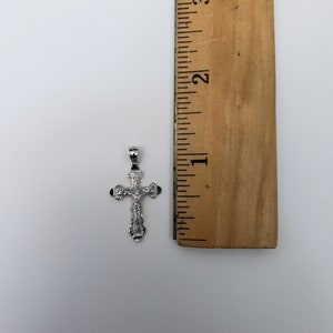 May include: A silver cross pendant with a detailed design, measuring approximately 2.5 cm in length. The cross is shown next to a ruler for size reference.