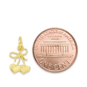 May include: Gold-toned cherry charm with a bow on top. The charm is about the size of a US penny.