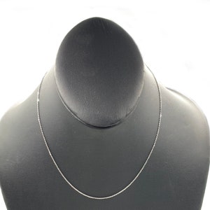 May include: A silver chain necklace on a black display stand.