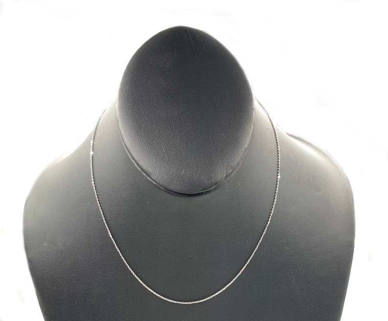 May include: A silver chain necklace on a black display stand.