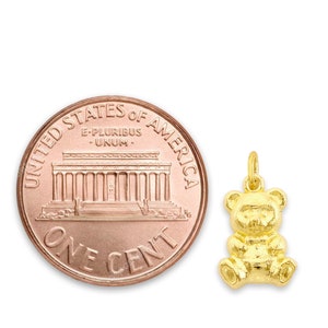 May include: A gold-colored teddy bear charm pendant, shown next to a US penny for size comparison.