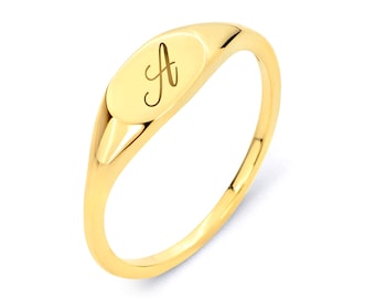 May include: A gold signet ring with a raised oval top featuring the letter 'A' engraved in a cursive script.