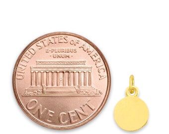 Puede incluir: Un colgante redondo dorado con un pequeño lazo para una cadena, junto a una moneda estadounidense de un centavo. La moneda es de color cobre y muestra el Lincoln Memorial. El colgante mide aproximadamente 1,3 cm de diámetro.