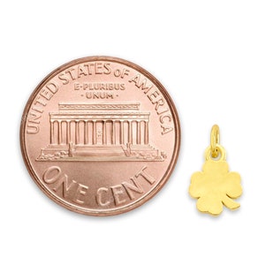 May include: A gold four-leaf clover charm pendant, shown next to a US penny for size comparison. The charm is a popular symbol of good luck and is perfect for adding a touch of whimsy to any jewelry piece.