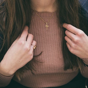 Puede incluir: Una mujer con un su&eacute;ter de punto marr&oacute;n con un collar de cruz dorada y un anillo dorado en el dedo.