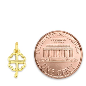Puede incluir: Un colgante de trébol de cuatro hojas de oro, que se muestra junto a un centavo estadounidense para comparar el tamaño.