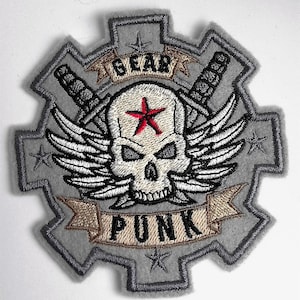Könnte beinhalten: Ein grauer gestickter Aufnäher mit einem Totenkopf und gekreuzten Knochen, Flügeln und einem Banner mit der Aufschrift "GEAR PUNK".