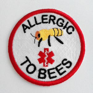 Könnte beinhalten: Gestickter Aufnäher mit weißem Hintergrund, rotem Rand und den schwarzen Worten "ALLERGIC TO BEES". Eine gelb-schwarze Bienen-Grafik befindet sich über einem roten medizinischen Symbol.