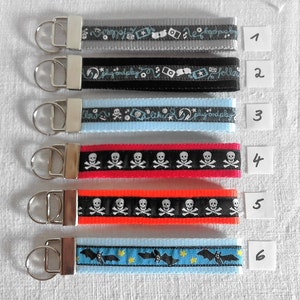 May include: Six different keychains with various designs. The keychains are made of black, gray, blue, red, and orange ribbon with different patterns. The keychains are numbered 1 through 6.