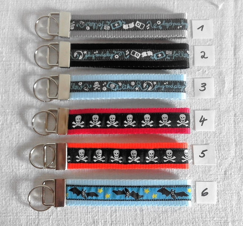 May include: Six different keychains with various designs. The keychains are made of black, gray, blue, red, and orange ribbon with different patterns. The keychains are numbered 1 through 6.
