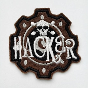 Könnte beinhalten: Brauner und schwarzer gestickter Aufnäher mit einem weißen Totenkopf, der eine Sonnenbrille trägt, und dem Wort "HACKER" in weißen Buchstaben.