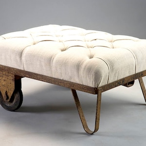May include: A white linen tufted ottoman with a metal frame and wheels. The frame is labeled "Novo Chef" and has a rusty finish.