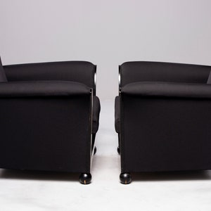 May include: Two black armchairs with chrome accents and black wooden legs. The chairs are upholstered in a black fabric with a subtle texture.