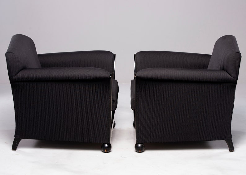 May include: Two black armchairs with chrome accents and black wooden legs. The chairs are upholstered in a black fabric with a subtle texture.