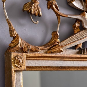 May include: A gold and white ornate mirror with a decorative floral design. The mirror has a beveled edge and a simple frame.