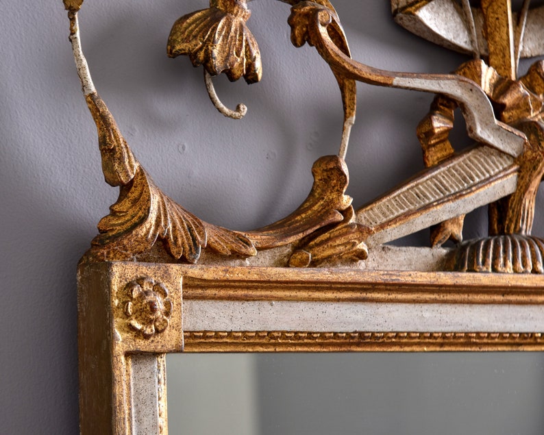 May include: A gold and white ornate mirror with a decorative floral design. The mirror has a beveled edge and a simple frame.