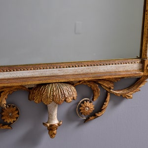 May include: A gold and white ornate mirror with a decorative carved frame. The frame features a central floral design and scrolling details.