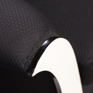 May include: Close-up of a black fabric armchair with a white curved armrest. The fabric has a textured woven pattern.