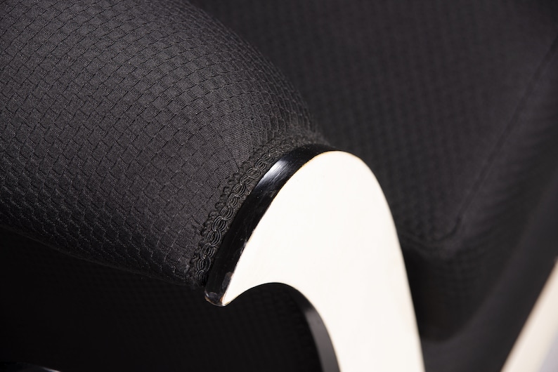 May include: Close-up of a black fabric armchair with a white curved armrest. The fabric has a textured woven pattern.
