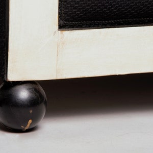 May include: Close-up of a black and white chair with a round black wooden leg. The chair has a white painted frame and black fabric upholstery.