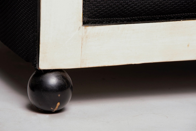 May include: Close-up of a black and white chair with a round black wooden leg. The chair has a white painted frame and black fabric upholstery.