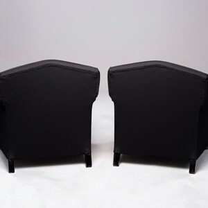 May include: Two black armchairs with tufted upholstery and wooden legs. The chairs are positioned back-to-back, showcasing their rear view.