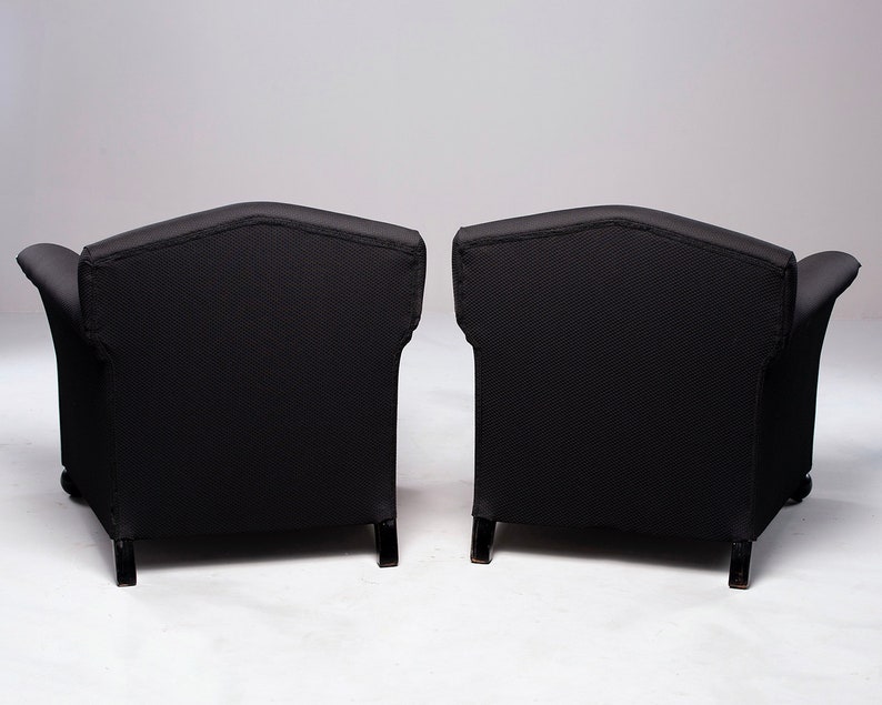 May include: Two black armchairs with tufted upholstery and wooden legs. The chairs are positioned back-to-back, showcasing their rear view.