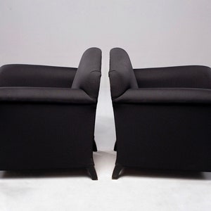 May include: Two black armchairs with tufted upholstery and wooden legs. The chairs are positioned side-by-side, facing forward.