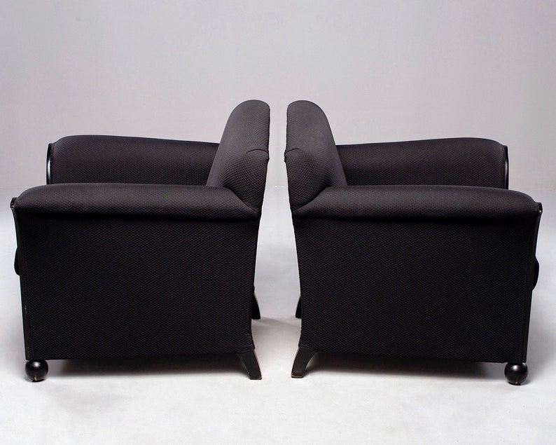 May include: Two black armchairs with tufted upholstery and wooden legs. The chairs are positioned side-by-side, facing forward.