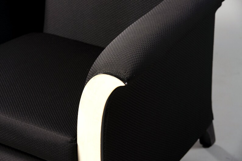 May include: Black armchair with a white curved armrest. The chair has a textured fabric upholstery.