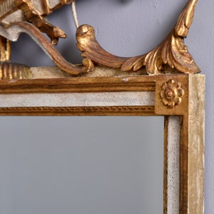 May include: A gold and white ornate mirror frame with a decorative top. The frame has a white base with gold accents and a gold top with intricate carvings.
