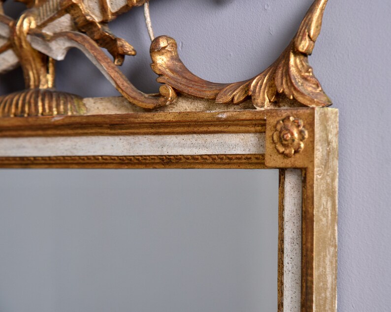 May include: A gold and white ornate mirror frame with a decorative top. The frame has a white base with gold accents and a gold top with intricate carvings.